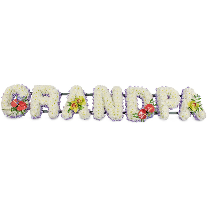 This photograph shows an elegant "GRANDPA" funeral flower tribute, arranged in a long horizontal line of sturdy block capitals, designed to rest on a stand or along the front of a coffin. Every letter is densely covered with small white chrysanthemums, meticulously placed so that no gaps appear, giving the surface a plush, cushion-like texture that softens the bold shapes. The flowers are a clean, bright white, their rounded petals catching gentle, even light against a plain studio background, which enhances the sense of purity and calm. Along the lower edge of the letters runs a band of light lavender ribbon, subtly visible beneath the blooms and adding a refined wash of pastel colour that gently frames the word. Dark green brackets and bars discreetly link the letters from behind, ensuring the piece remains secure for transport and display at funeral venues in and around Limehouse. Splashes of richer colour are placed thoughtfully across the tribute: the "G" and "D" are adorned with striking clusters of deep red anthuriums, their polished, heart-shaped forms and golden spadices arranged with glossy foliage and hints of purple filler flowers, evoking love, courage, and deep respect. The first and last "A" are softened with sprays of yellow-green orchids, their arching stems, patterned throats, and vibrant yet gentle hue bringing a whisper of hope and enduring connection. The overall impression is of a bespoke, lovingly crafted memorial, ideal for families along the Limehouse Cut or near Narrow Street who wish to celebrate a grandfather's life with a tribute that combines traditional white sympathy flowers with meaningful touches of colour and character.