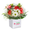 Vivid and inviting, this joyful bouquet evokes the spirit of a clear morning by Limehouse Marina, shining from within a simple, elegant white gift bag. Coral and peach carnations, bursting with soft, layered petals, infuse gentle warmth and energy into the heart of the composition. Lively white daisies, accented by sparkling yellow-green centers, dance alongside, infusing the arrangement with a crisp brightness reminiscent of early London springtime. Wisps of tiny, starry baby's breath float gracefully between the blooms, adding a dreamy airiness unique to carefully made florals. The ensemble is gently framed with broad, radiant green leaves-deeply verdant and just touched by light-forming a lush foundation that hugs the bouquet with a sense of security and devotion. On the left edge, partially hidden buds tinged in purple hint at surprises yet to open, lending a sense of curiosity to the design. Satin white ribbon handles crown the square bag, making the bouquet ready for cheerful gifting-whether delivered to an office on Westferry Road or a welcoming home near Narrow Street. Captured against a flawless white background, the bouquet radiates clarity and brightness, inviting the senses to linger over each blossom and thoughtful detail. Every element, from petal to leaf, is placed with intent, reflecting the pride and creative flair of Limehouse's local floral experts-a perfect arrangement for new beginnings, celebrations, or simply lighting up someone's day nearby.